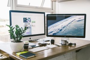 A desktop with a Mac computer, a plant, and several office supplies.